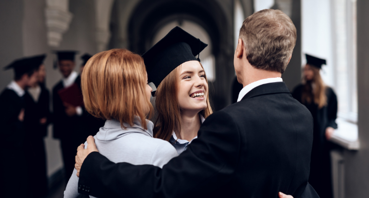 Woman and man embracing a college graduate in a cap and gown