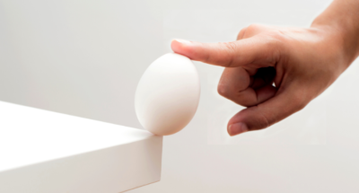 egg balanced by a finger at the corner of a white table